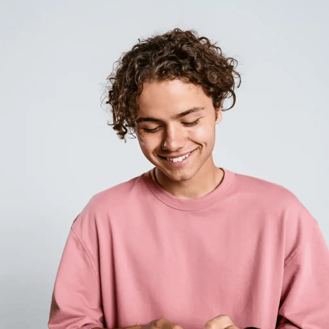 Guy with a smile in a pink sweater looking at phone