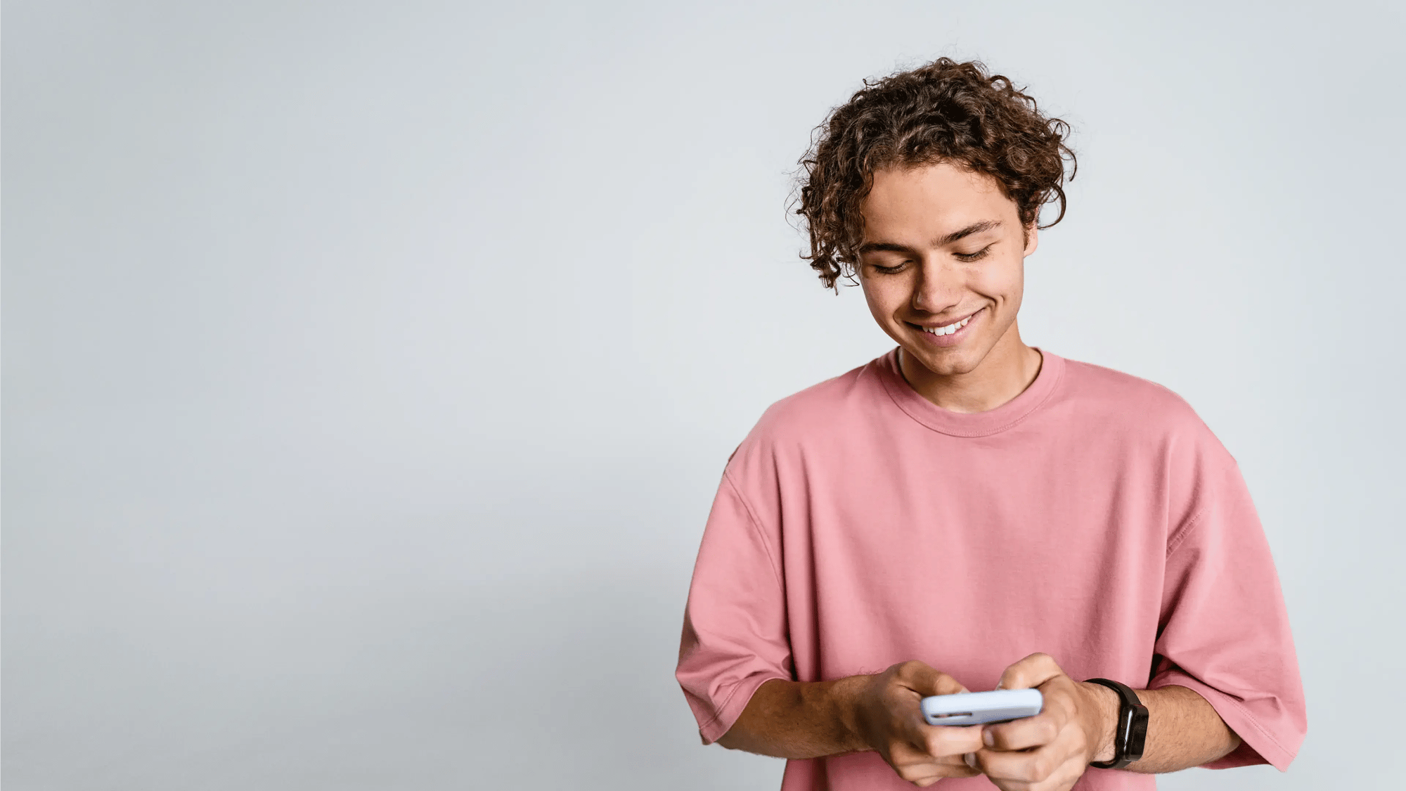 Young man in a pink t-shirt smiling while looking at his phone