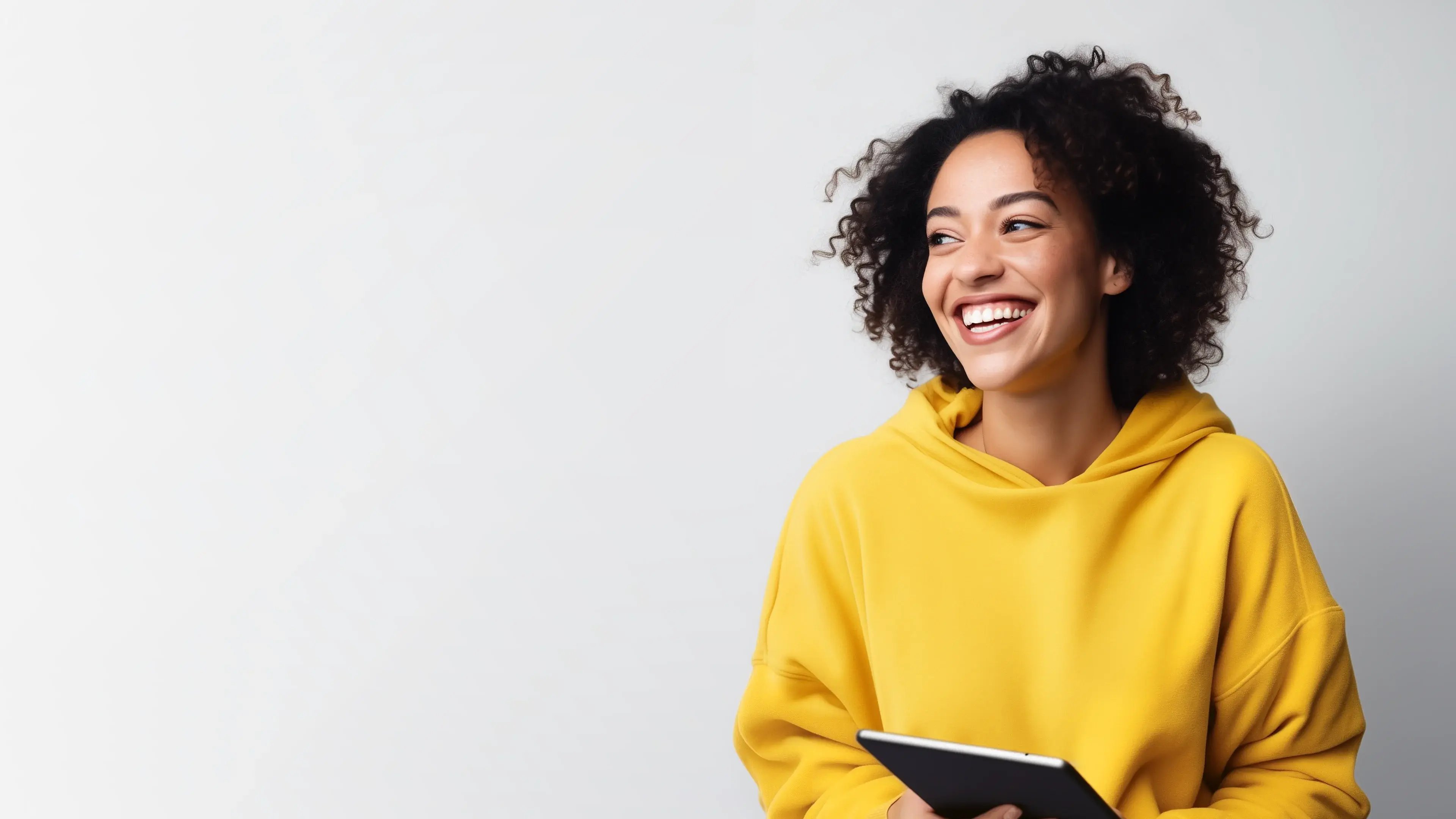 Smiling woman in a yellow hoodie holding a tablet against a light background